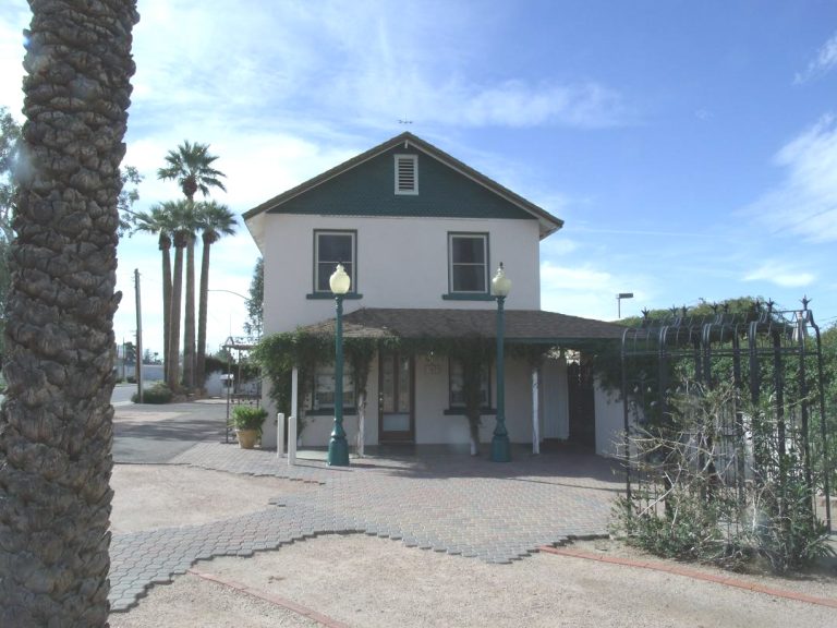 Two-story historic home with a shingle roof, iron fence and palm trees in Mesa, Arizona